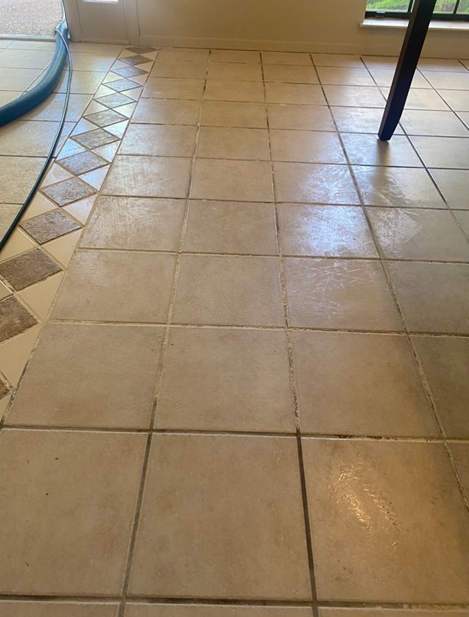 Beige tiled floor with dark grout, being cleaned with a vacuum.