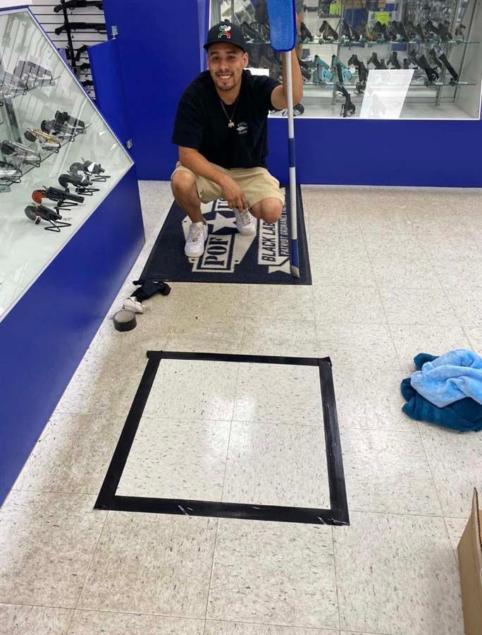 Man squatting with mop in shoe store, over a marked square.