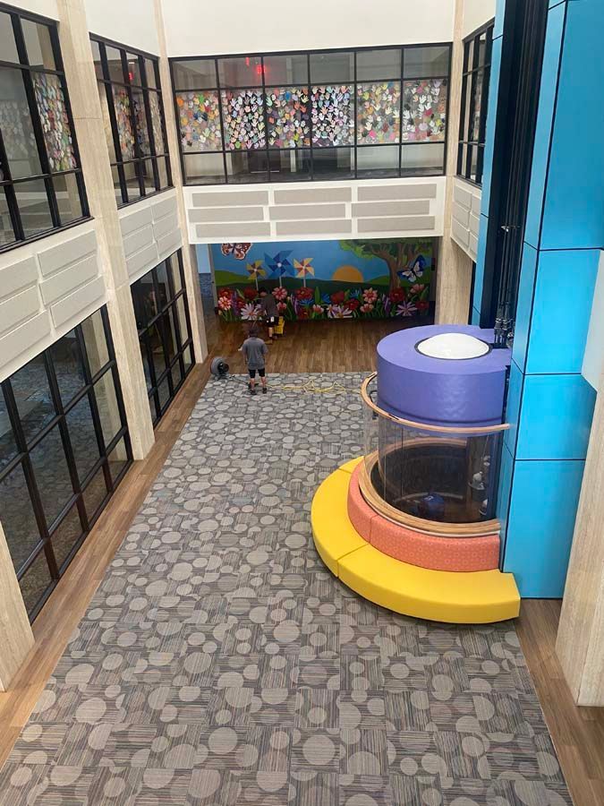 Elevated view of a colorful children's play area. Features a tall blue lift, grey flooring, and a floral mural.