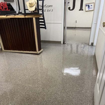 Inside a store with shiny, speckled floors, a wood-paneled counter with a hat and doorway visible.