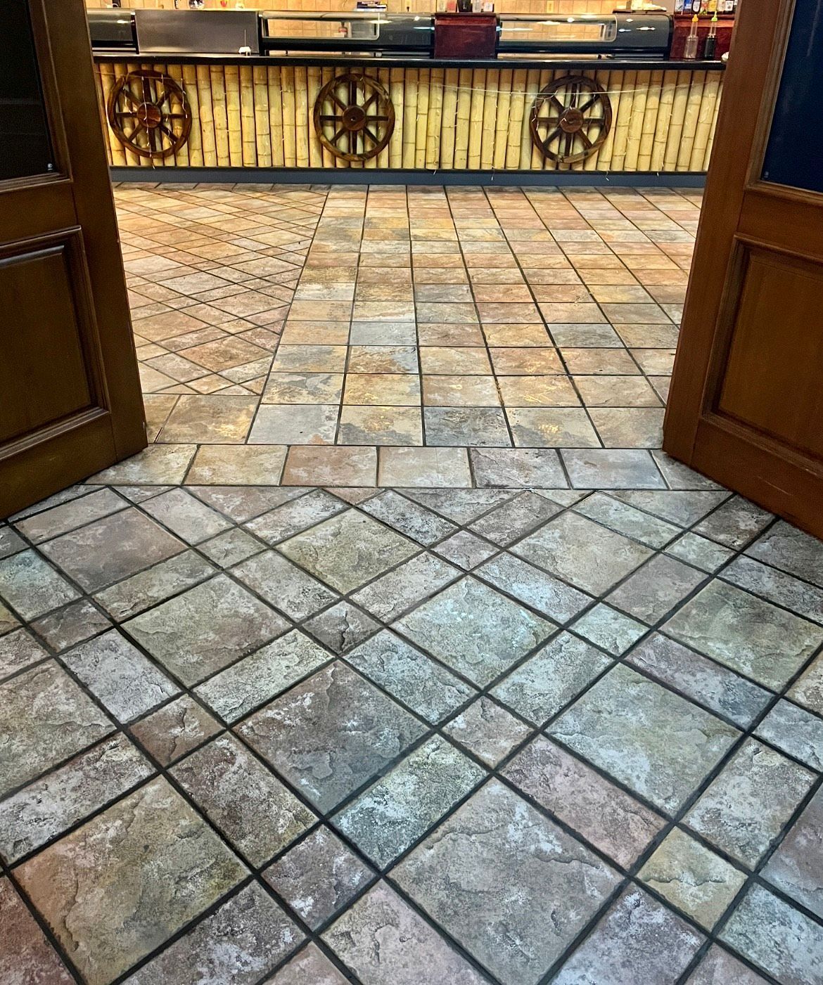 View through open wooden doors into a room with patterned tile flooring. A bamboo-decorated bar is visible in the background.