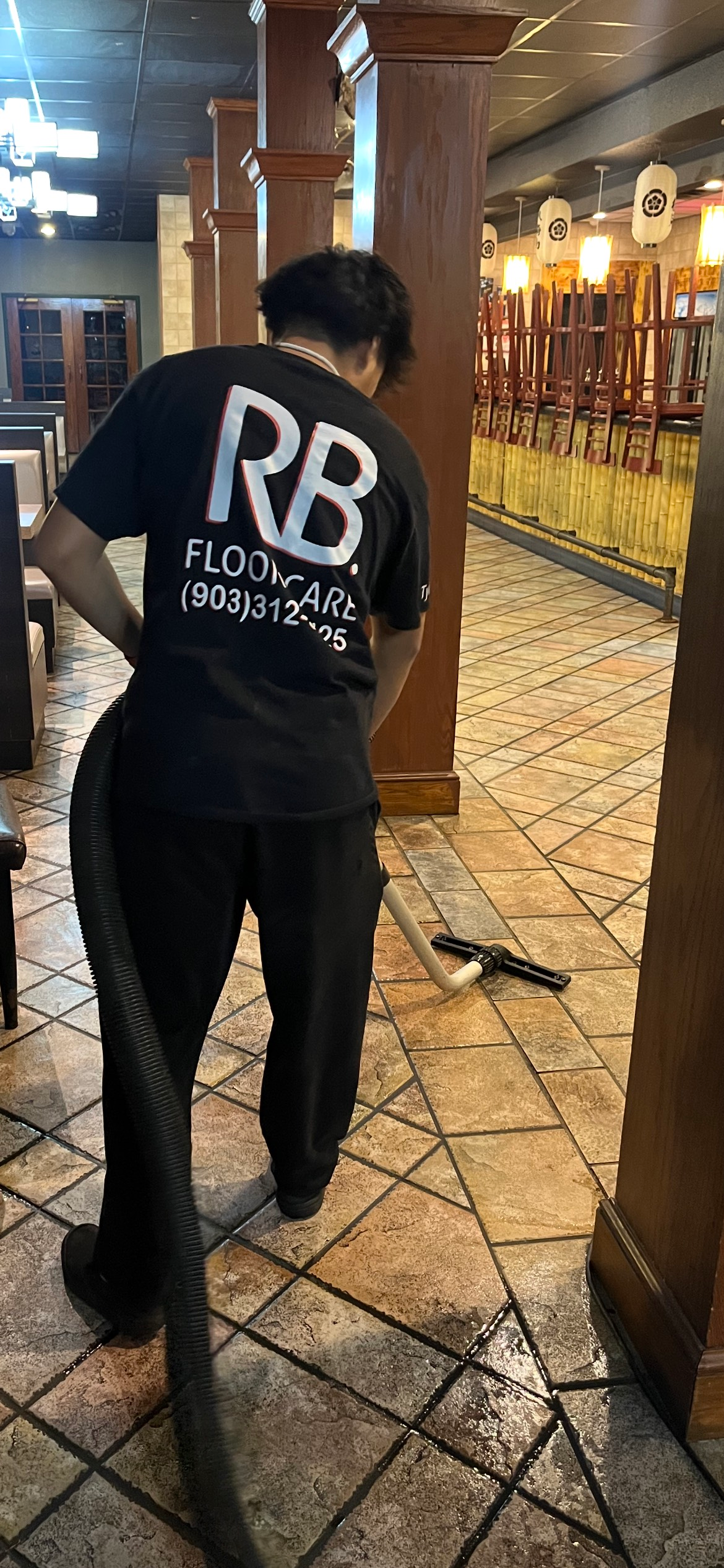 Person cleaning tiled floor with a vacuum. Restaurant setting.