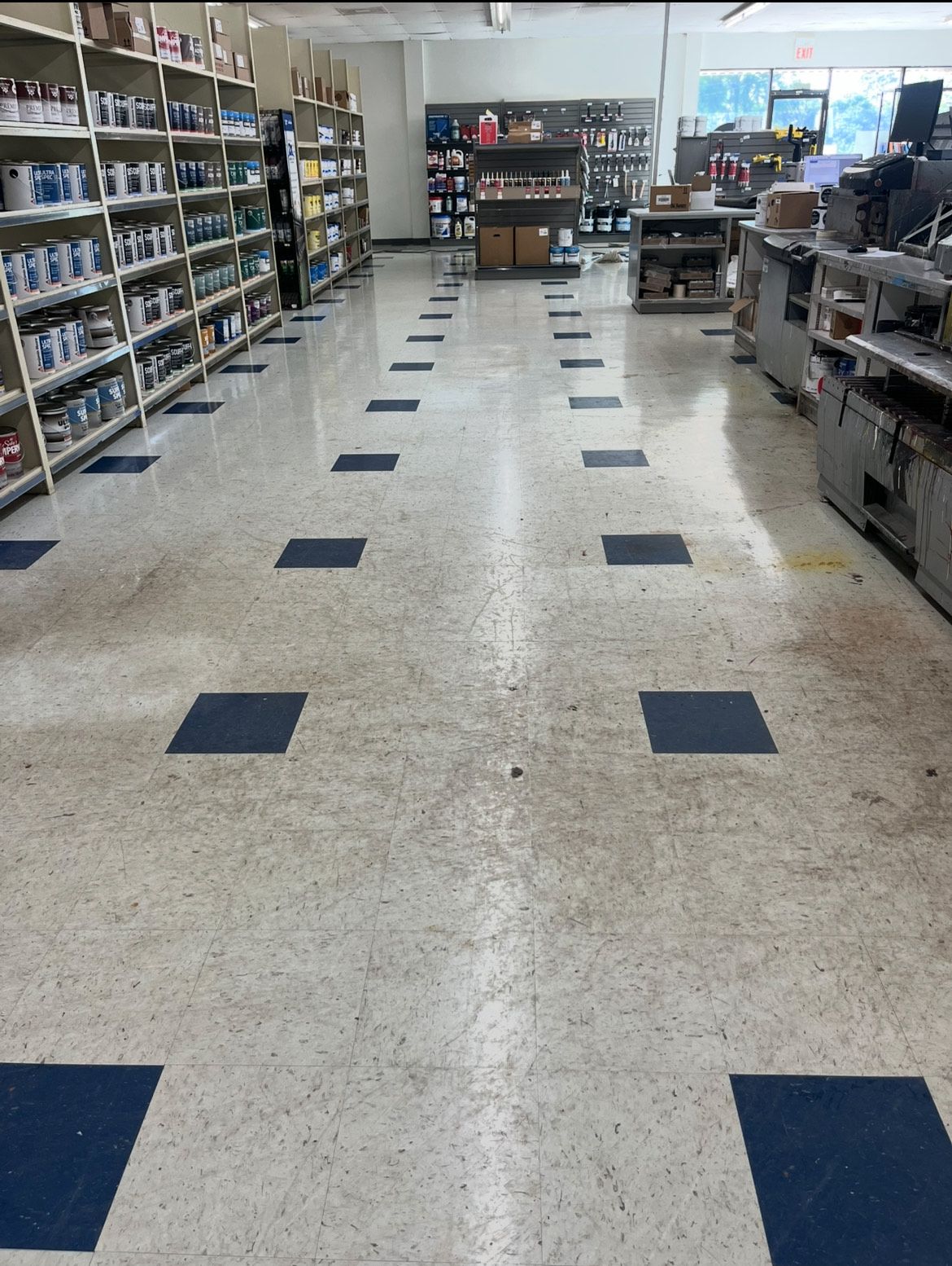 Interior of a store aisle with white and blue square tile flooring and shelves stocked with products.