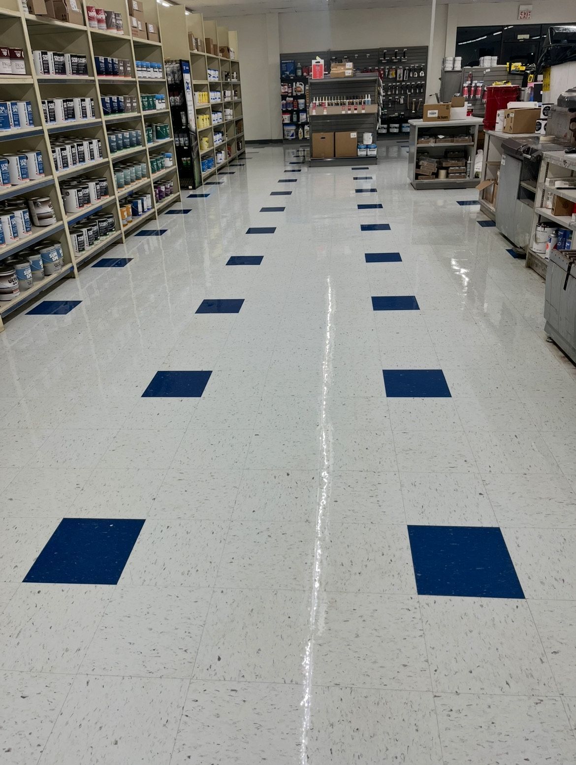 A retail store aisle with white speckled floor and blue square accents, shelving with products on either side.
