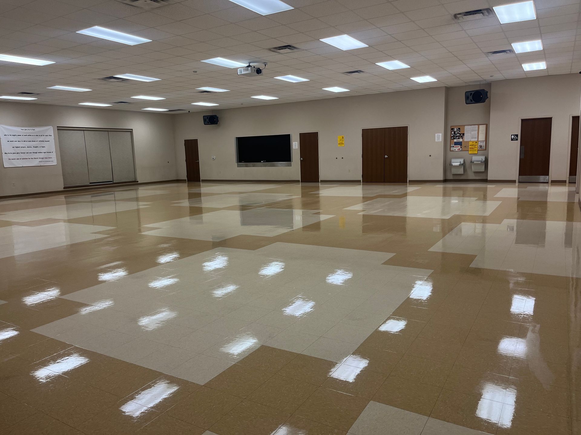 Empty community center room with shiny floor, doors, and overhead lights.