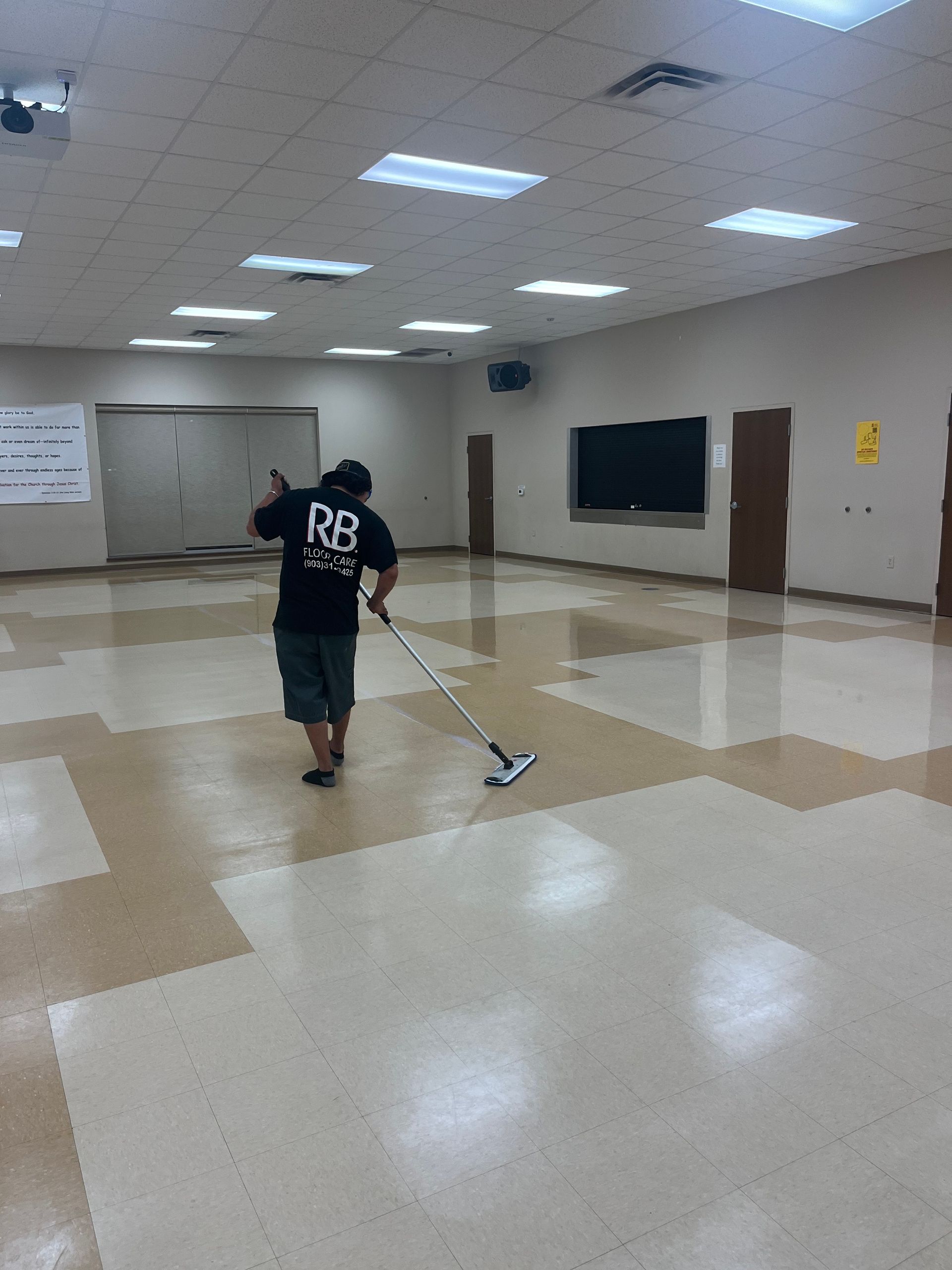 Person vacuums a large, empty room with beige and white patterned floor.