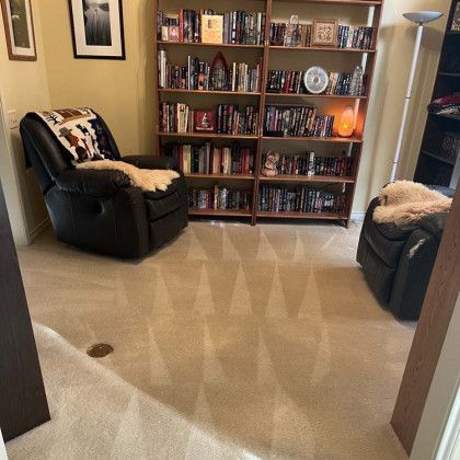 Cozy reading corner with two leather recliners, a bookshelf, and soft beige carpet.