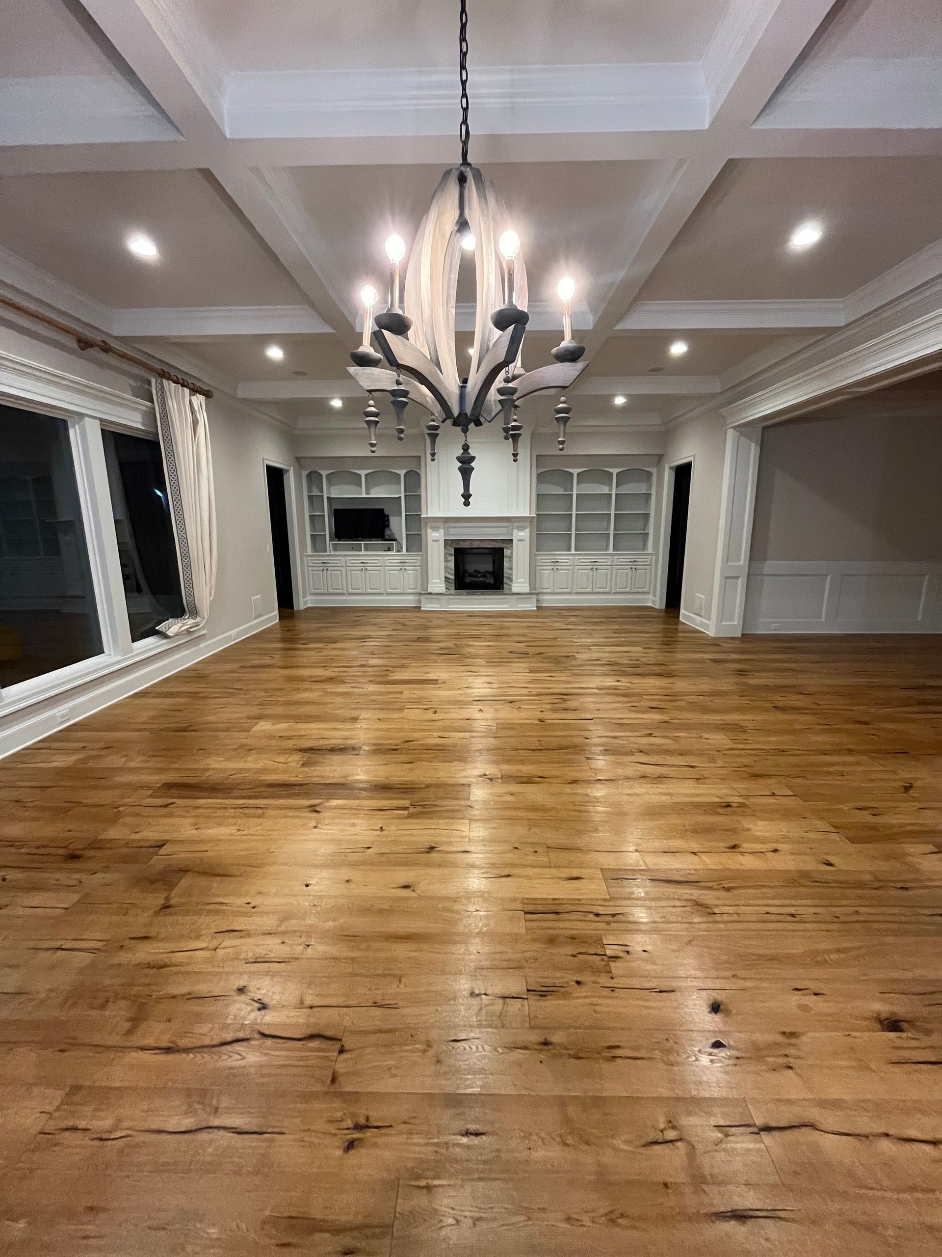 Empty, spacious living room with wood floors, a fireplace, and a chandelier.
