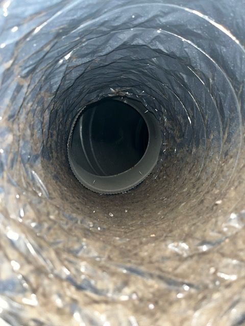 Inside view of a dirty HVAC vent. Light gray dust and debris coating flexible duct.