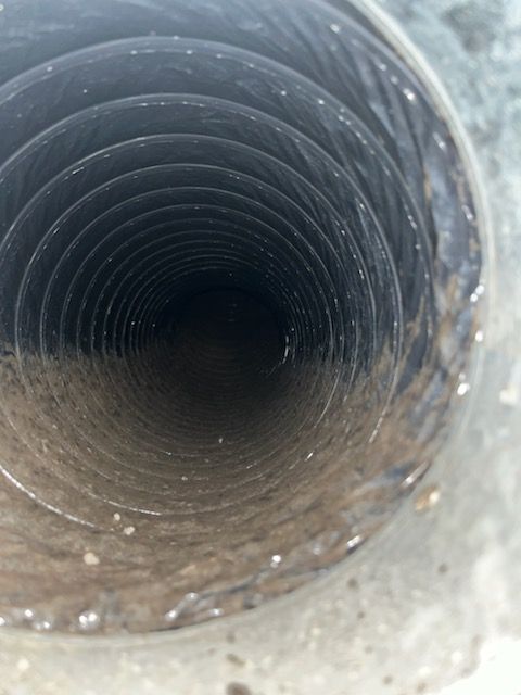 Inside view of a dirty, circular ventilation duct. Dark with dust and debris coating the walls.