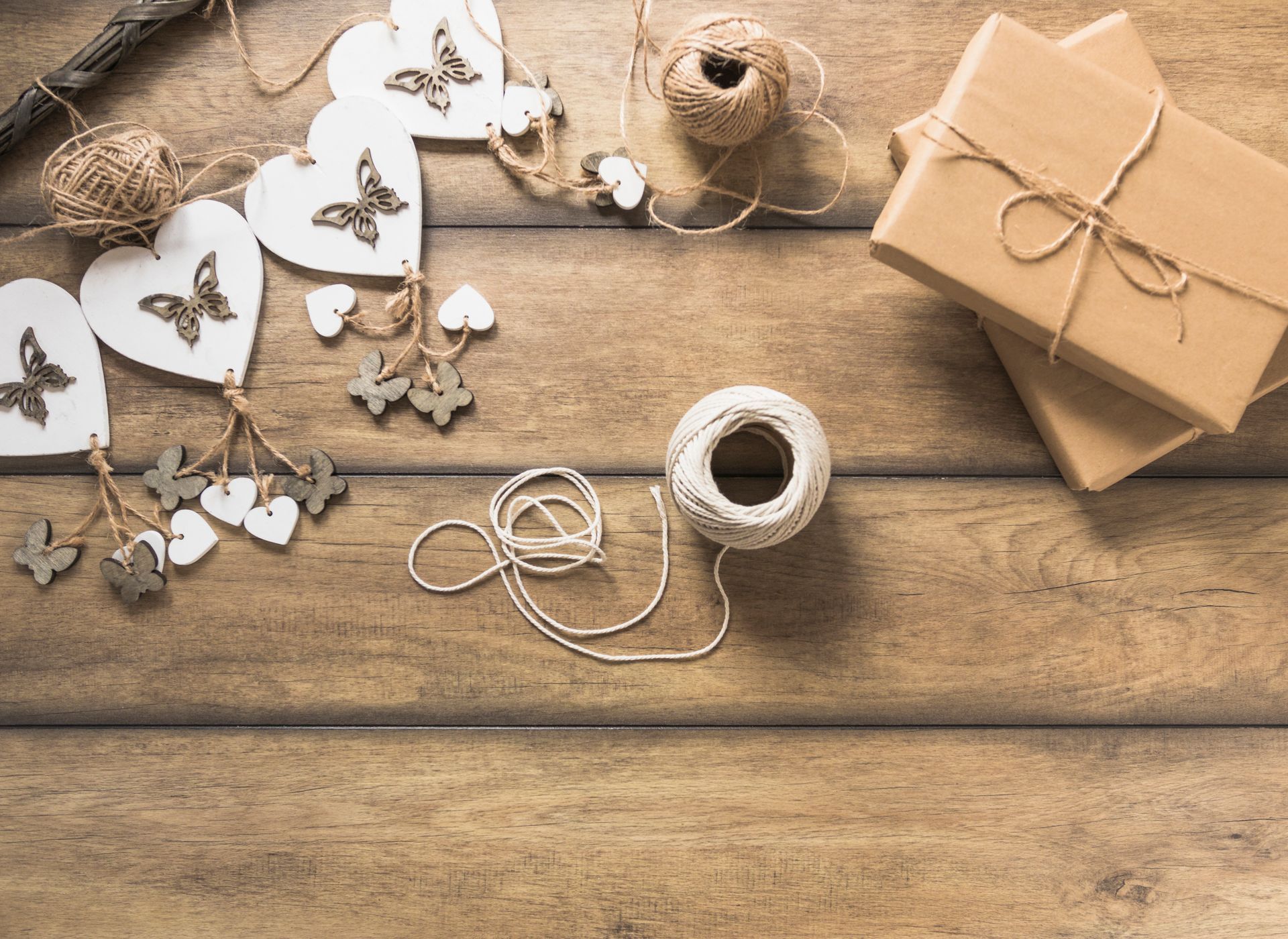 Paquetes marrones atados con cordel junto a corazones de madera decorativos y carretes sobre una superficie de madera.