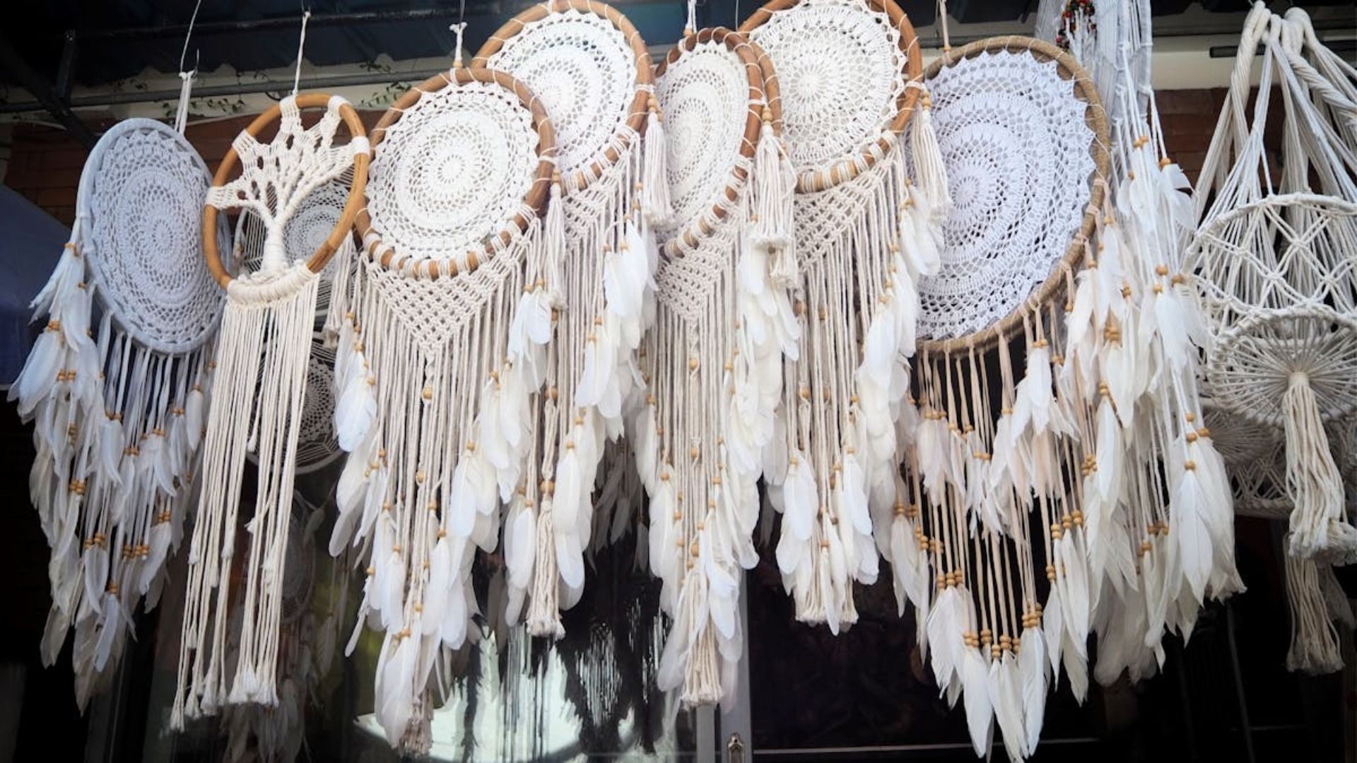 Colección de atrapasueños colgantes de color crema y tostado, decorados con plumas y patrones tejidos.