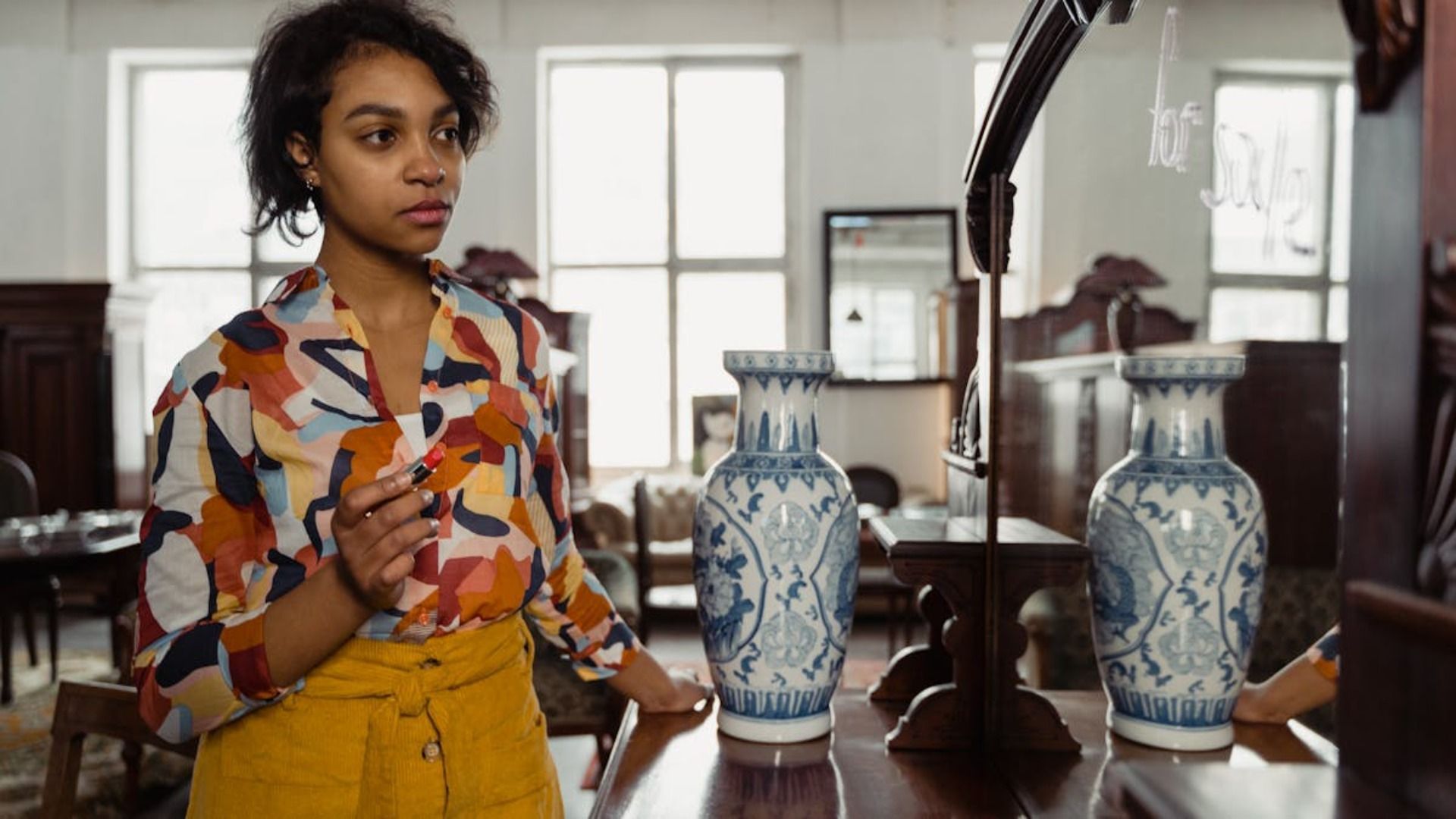 Una mujer con una camisa colorida mira dos jarrones azules y blancos en una tienda vintage.
