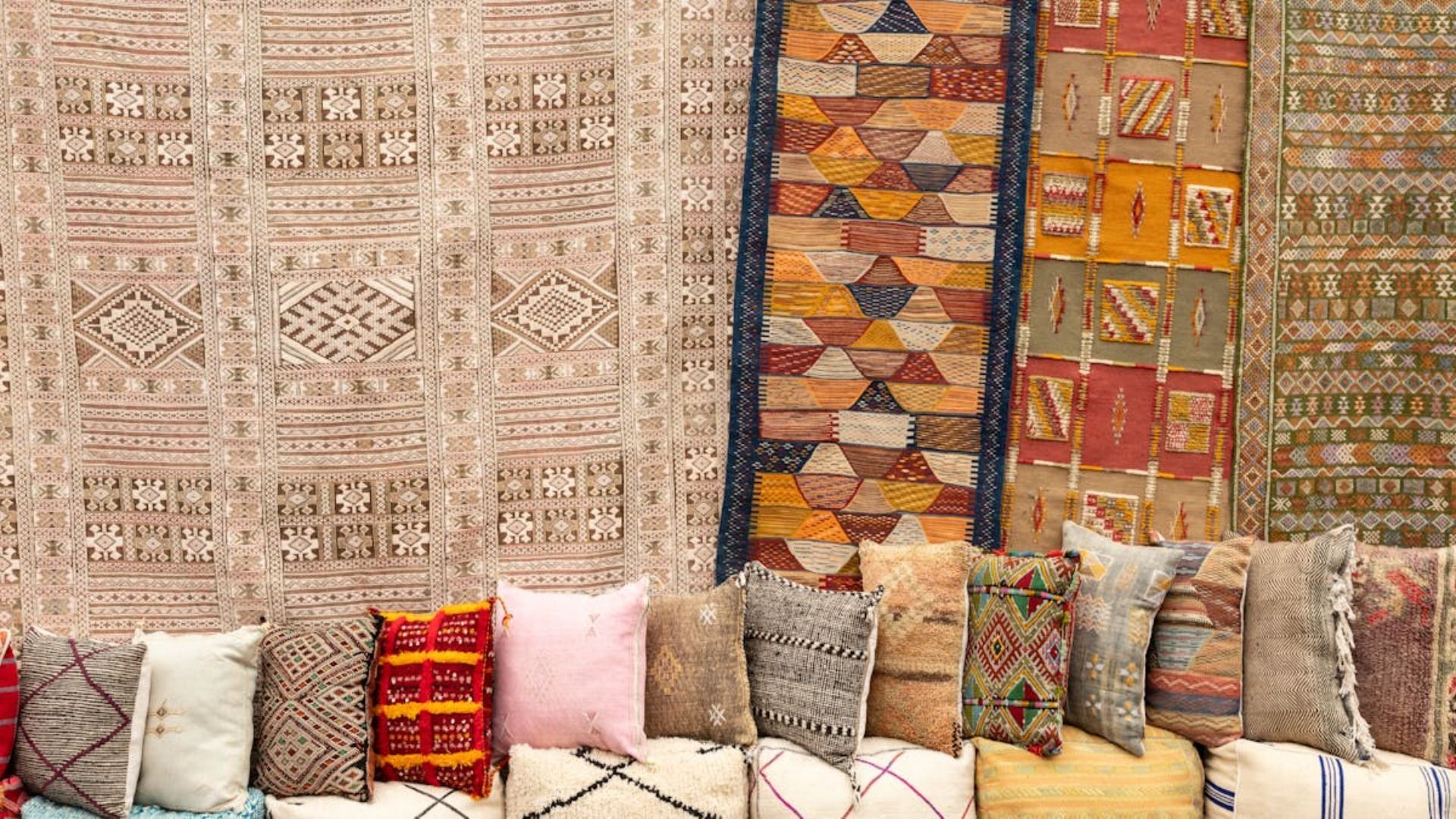 Venta de diversas alfombras y almohadas estampadas, con tonos tierra y diseños geométricos.