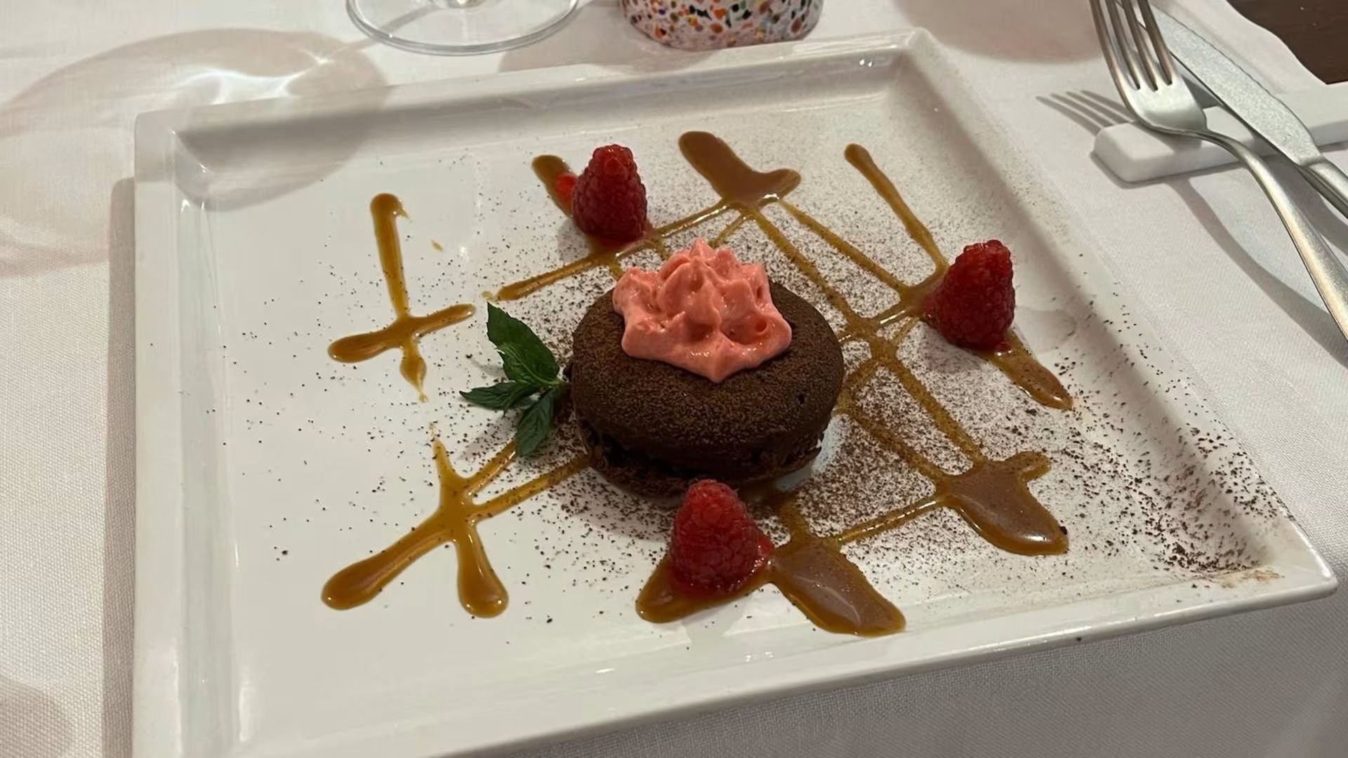 Dessert al cioccolato con crema rosa e guarnizione di frutti di bosco su un piatto bianco, irrorato con salsa.