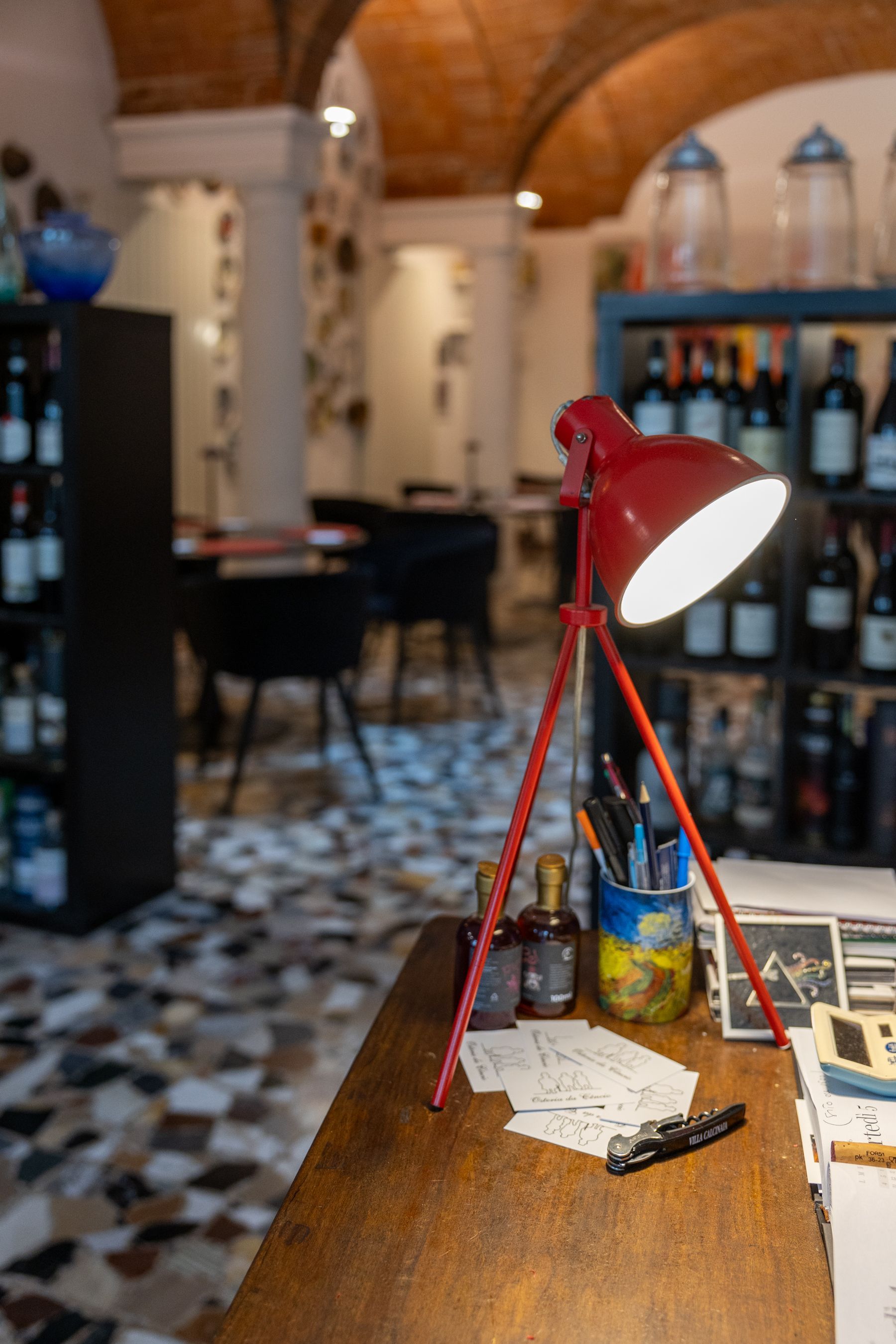 Lampada da scrivania rossa su un tavolo di legno in un ambiente caldo e illuminato, tipico di un caffè o di un bar.