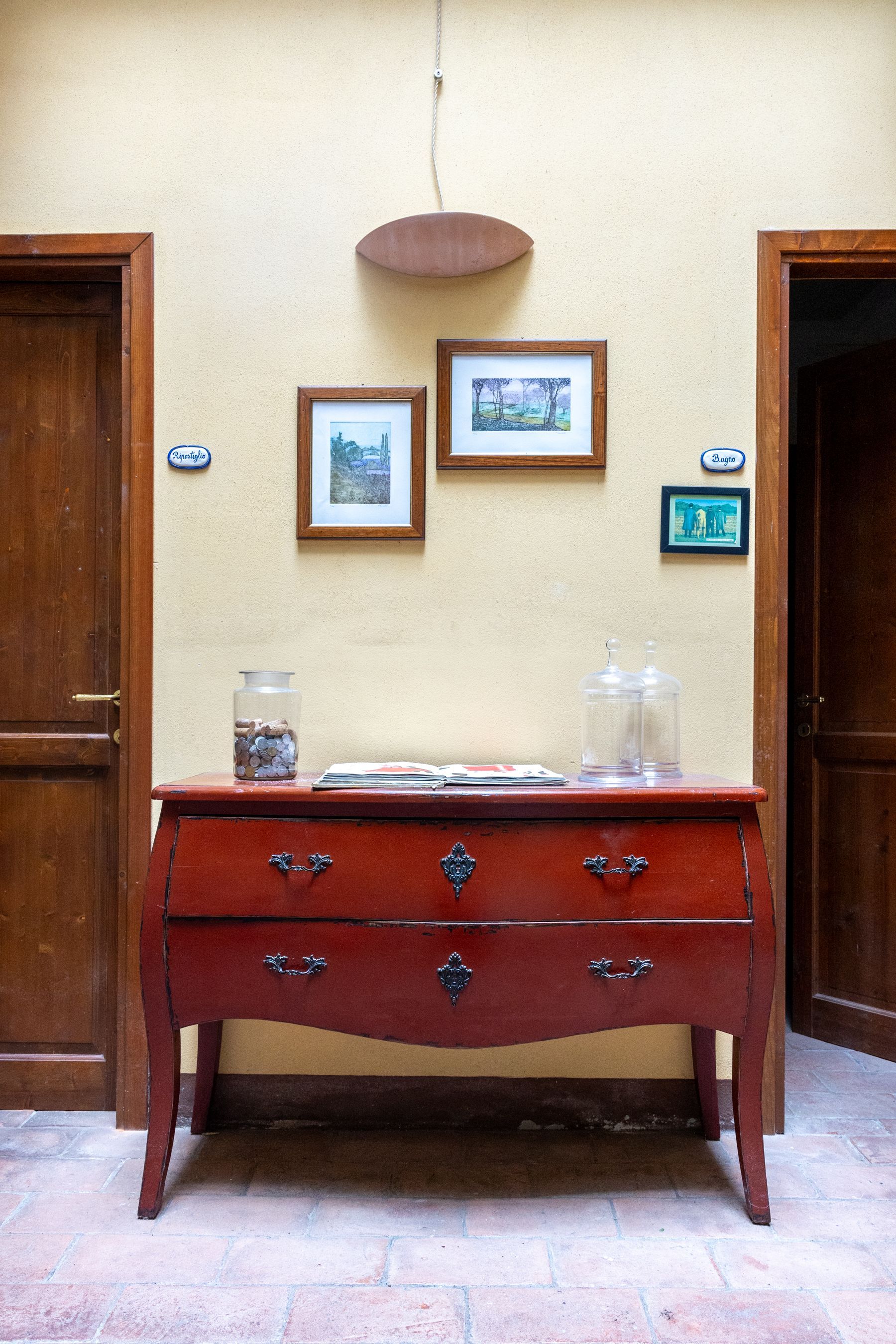 Credenza in legno con quadri incorniciati su una parete beige tra due porte.