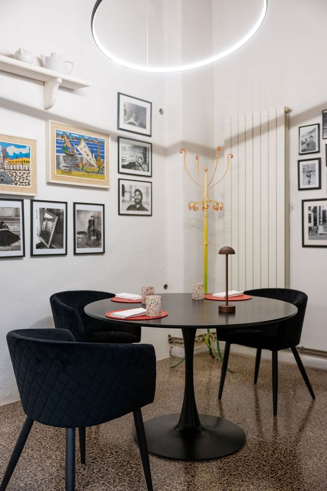 Angolo caffè moderno con tavolo rotondo nero, sedie scure, quadri appesi alle pareti e una luminosa lampada circolare a soffitto.