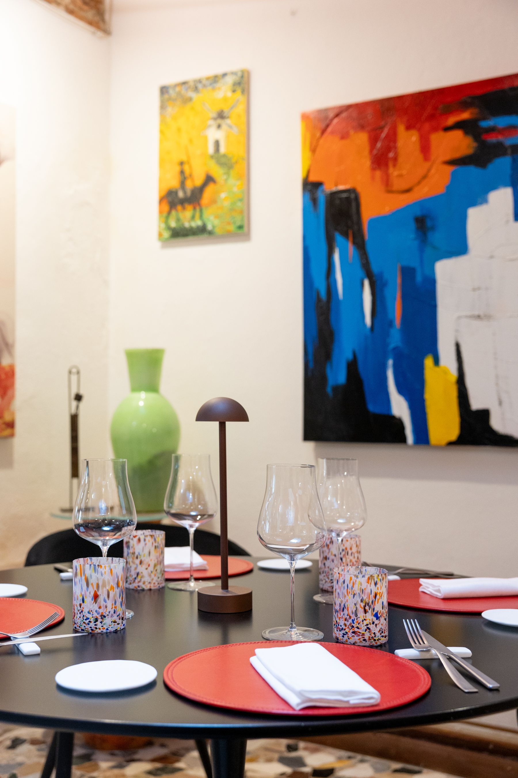 Tavolo da pranzo apparecchiato per un pasto in una stanza colorata e ricca di opere d'arte, con dipinti astratti alle pareti.