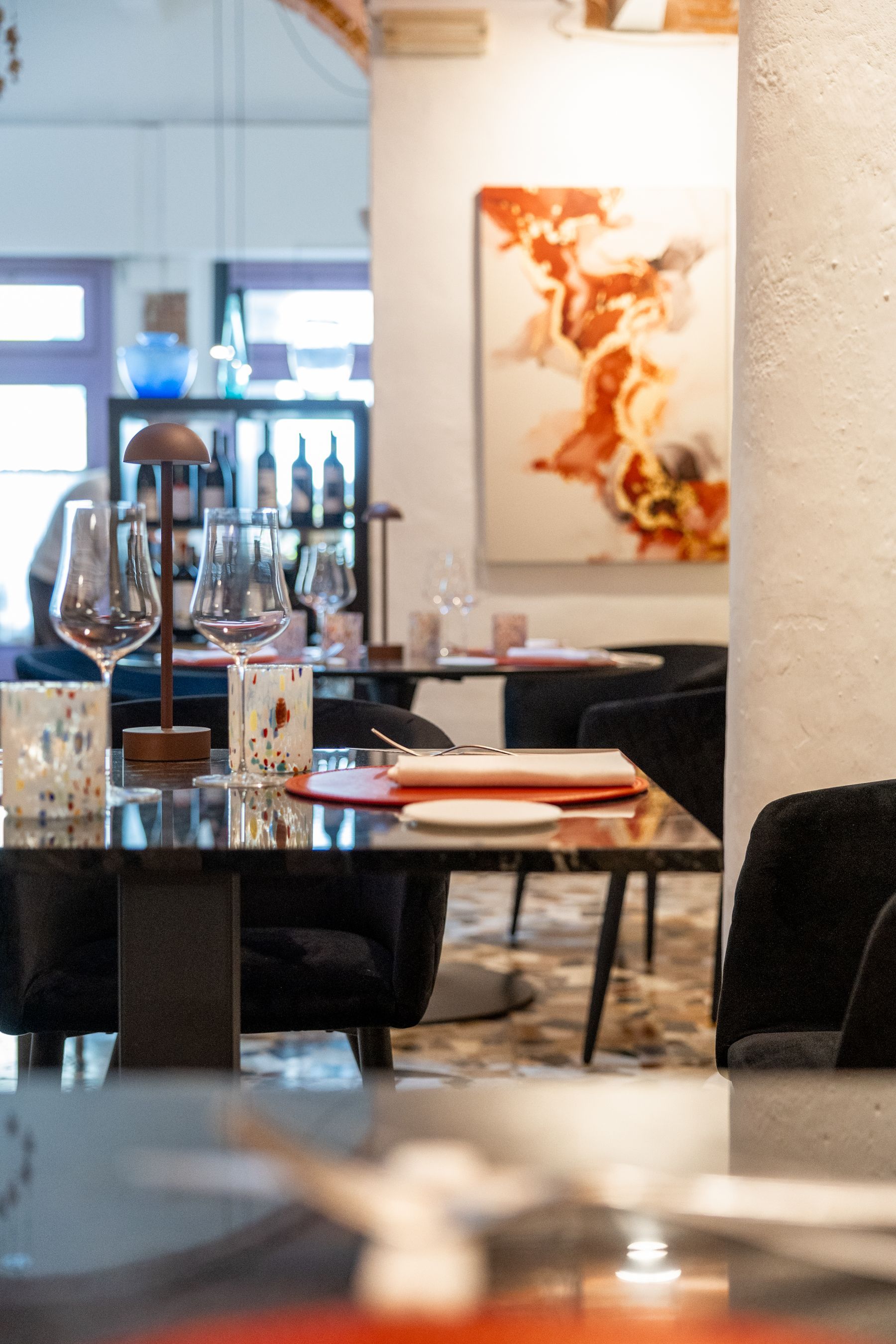 Elegante interno di ristorante con tavoli apparecchiati, calici da vino e opere d'arte astratte alle pareti.