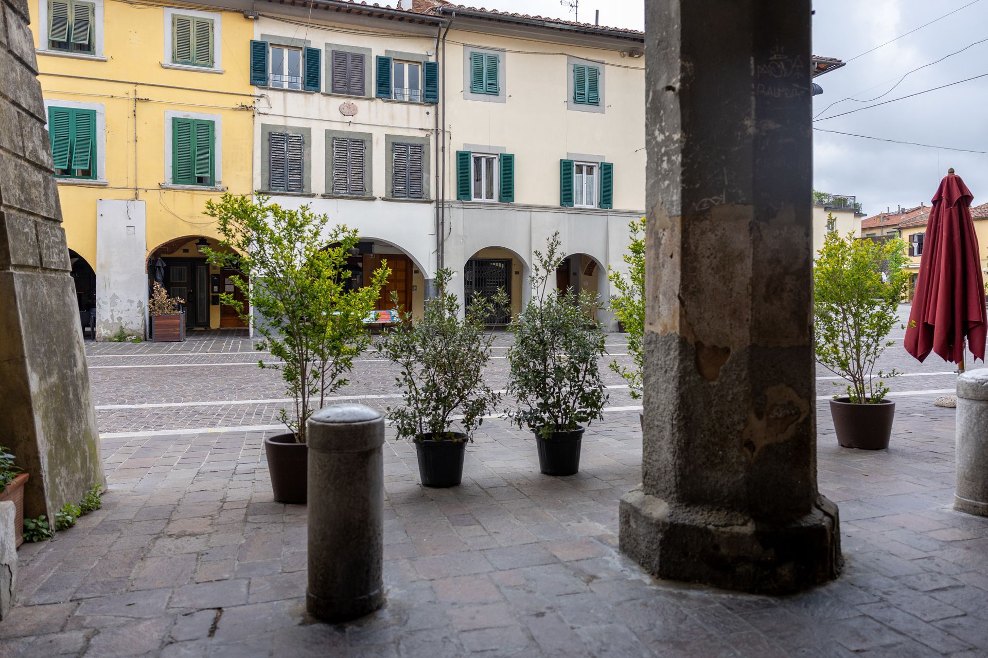 Portico in pietra affacciato su una piccola piazza in stile europeo con piante in vaso e edifici gialli dall'altra parte della strada