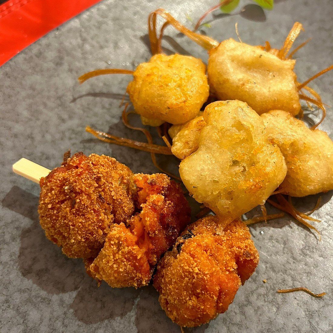 Spiedini di piccoli snack fritti, dorati e bruno-rossastri, in formato bocconcino, su una superficie grigia.