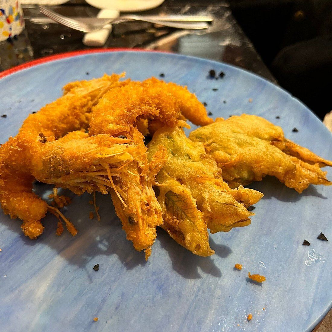 Piatto di gamberi fritti dorati su un piatto blu, con le posate sullo sfondo.