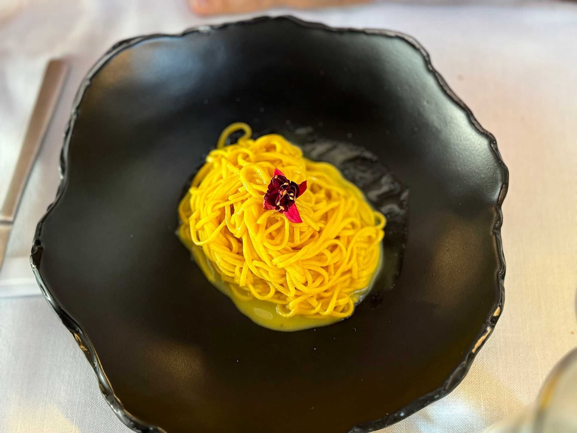 Ciotola nera con spaghetti gialli e una piccola guarnizione rossa al centro.