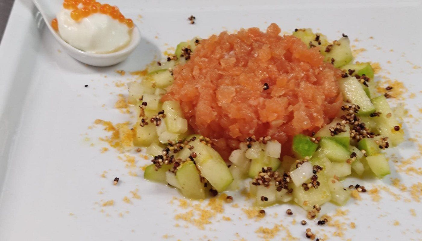 Avocado a cubetti condito con salsa di pomodoro, guarnito con semi di sesamo e una cucchiaiata di panna su un piatto.