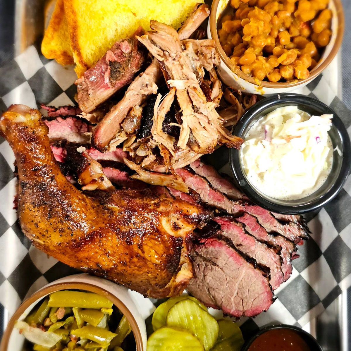 A tray of meat , beans , pickles and bread on a checkered paper.