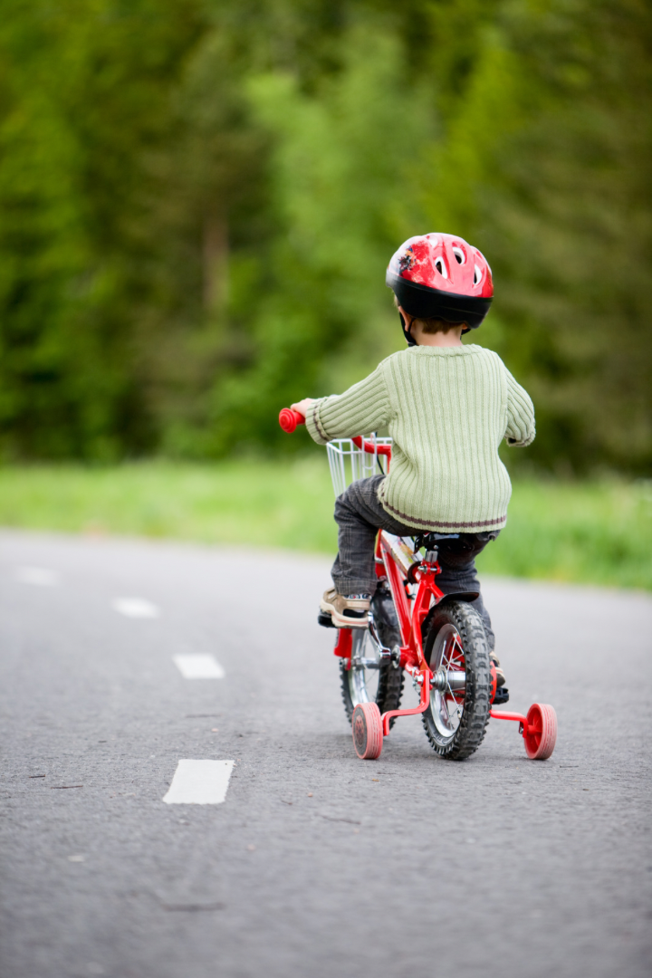A young boy is riding a red bicycle on a road.