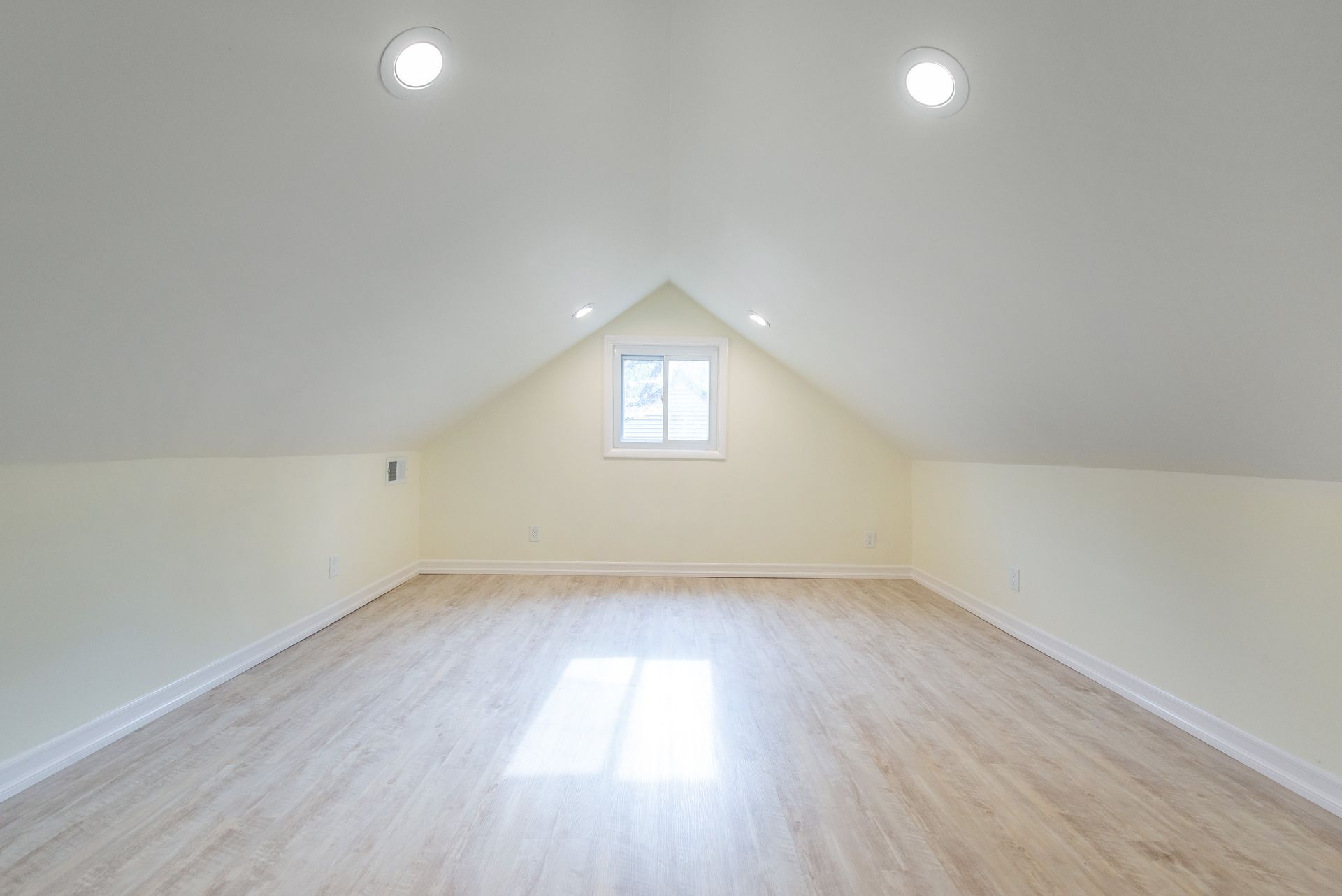 An empty attic with hardwood floors and a window.