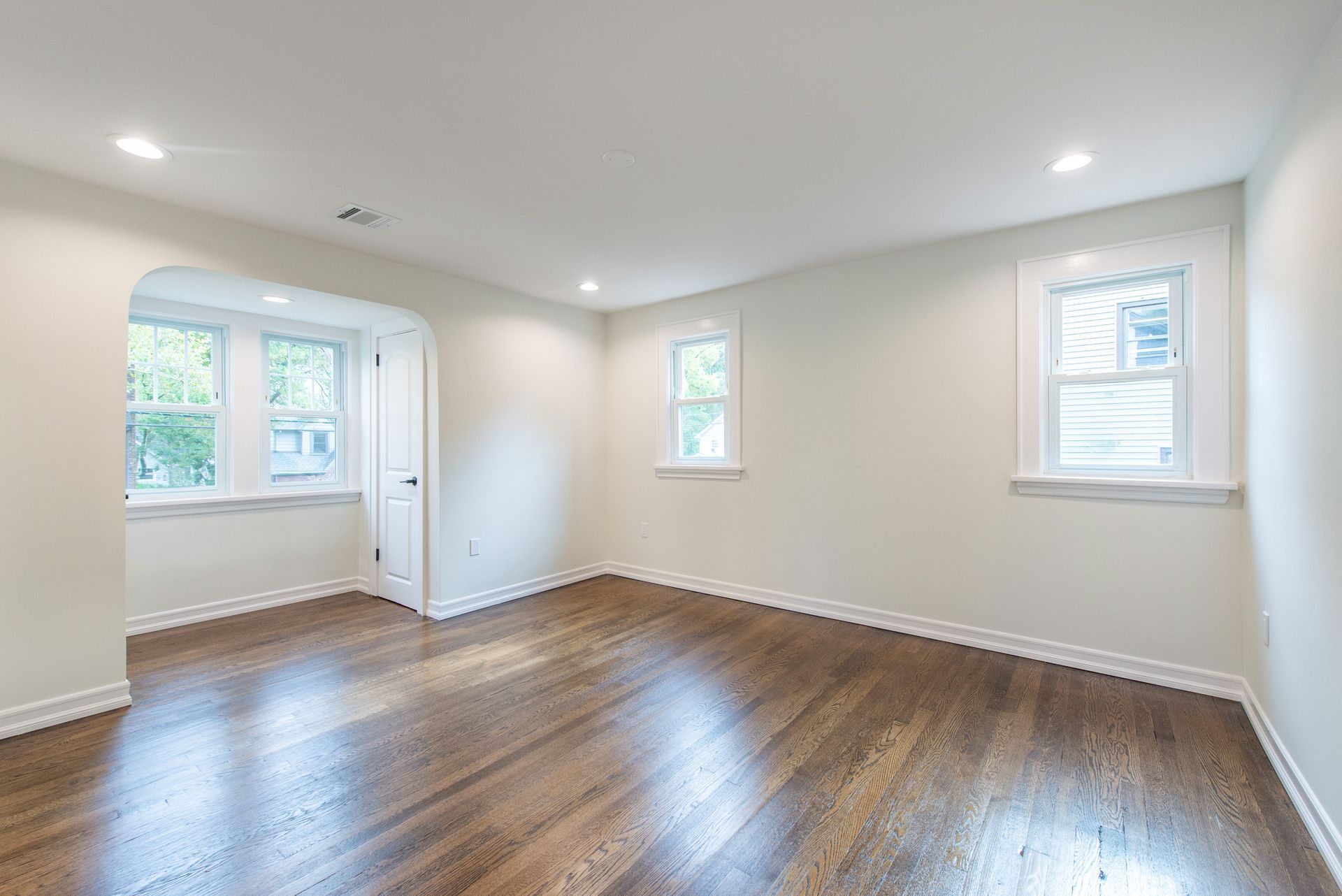 An empty living room with hardwood floors and white walls.
