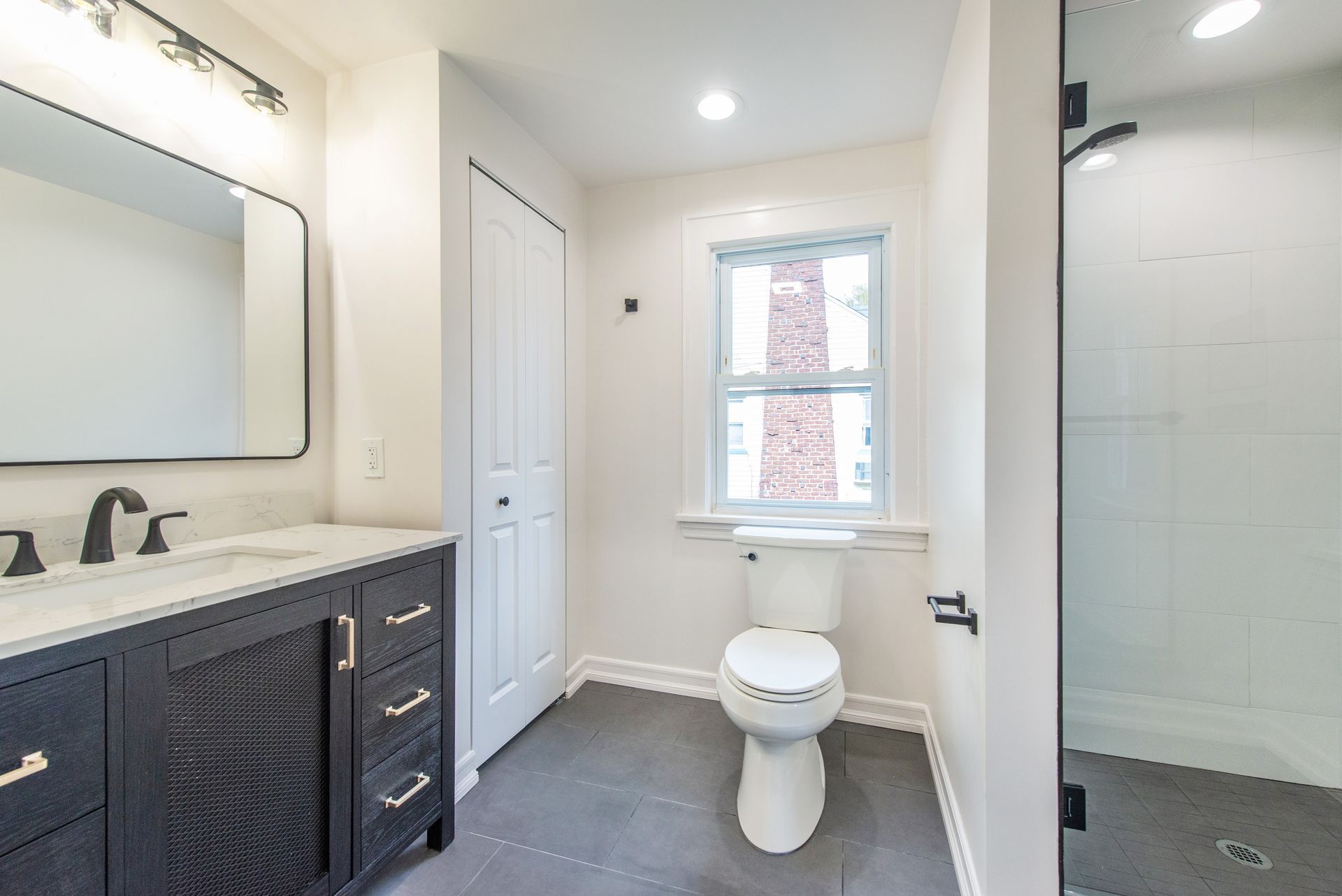 A bathroom with a toilet , sink , mirror and walk in shower.