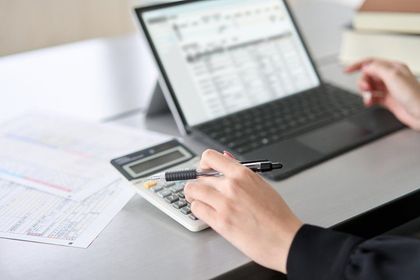 A person is using a calculator in front of a laptop computer.