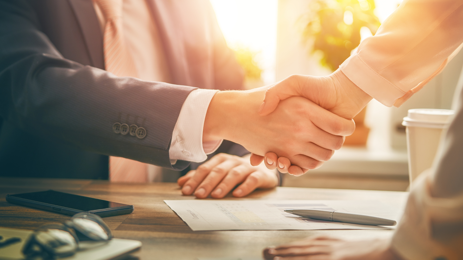 A man and a woman are shaking hands over a table.