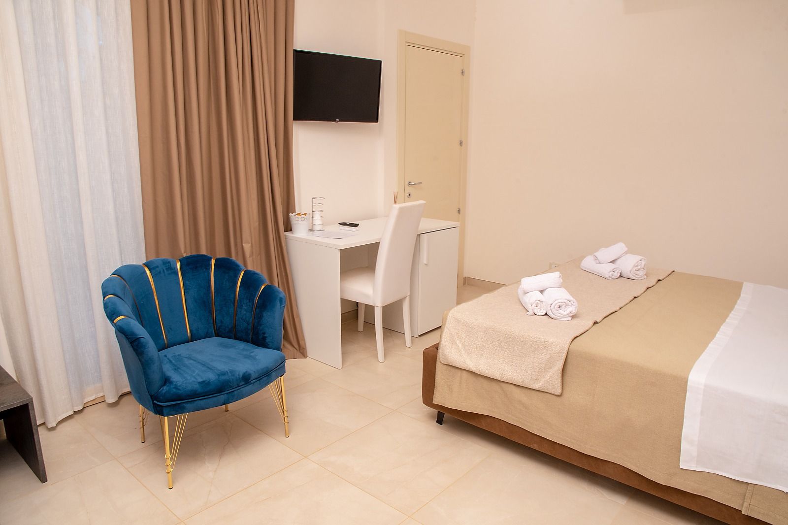 Camera d'albergo con letto, scrivania, sedia blu e tende.