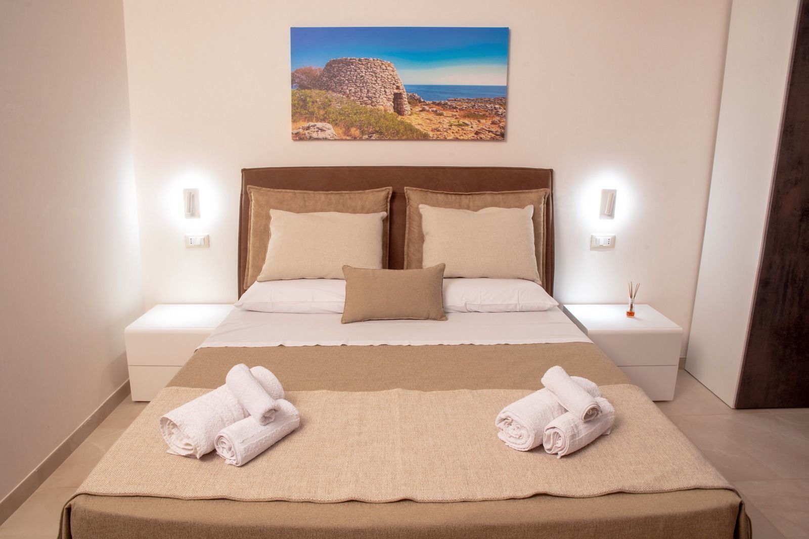 Camera da letto con letto fatto, comodini bianchi e dipinto di paesaggio. 