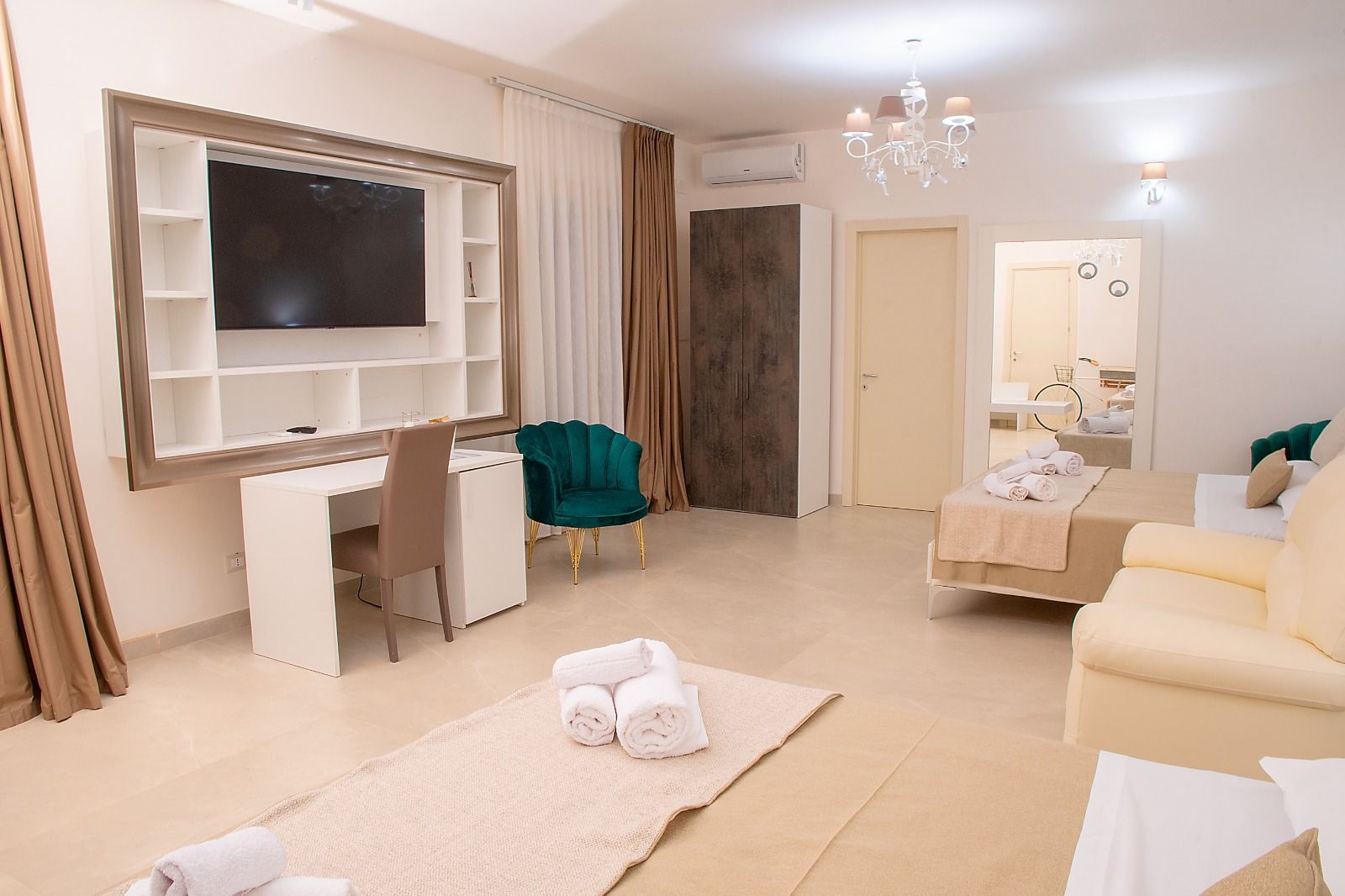 Ampia camera d'albergo con TV, scrivania, letto e zona salotto con dettagli verdi e beige.