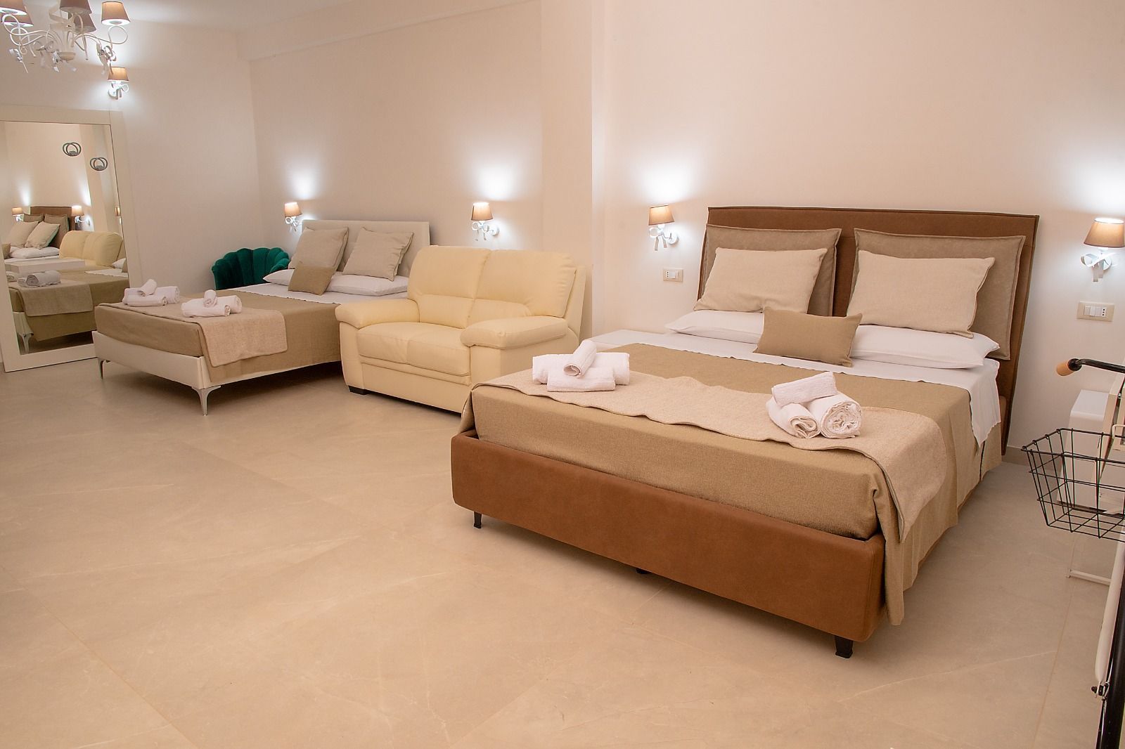 Ampia camera d'albergo con due letti, un piccolo divano, tonalità neutre e luci soffuse.