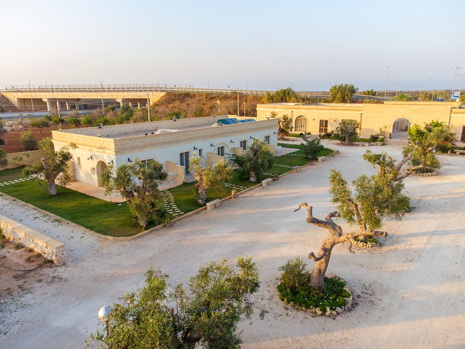 Edifici con portali ad arco e ulivi su un vialetto di ghiaia bianca.