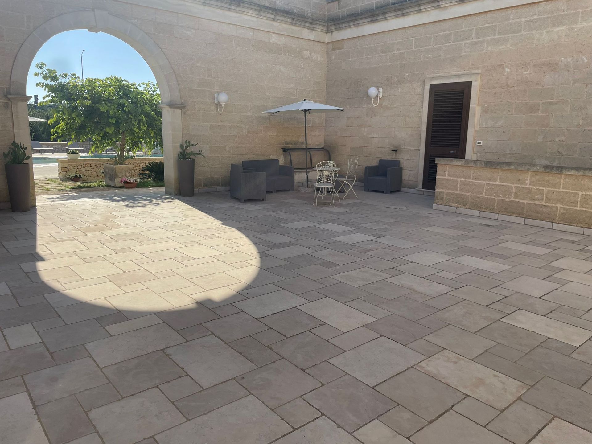 Un patio in pietra con posti a sedere sotto un ombrellone e un ingresso ad arco che conduce a un'area esterna.