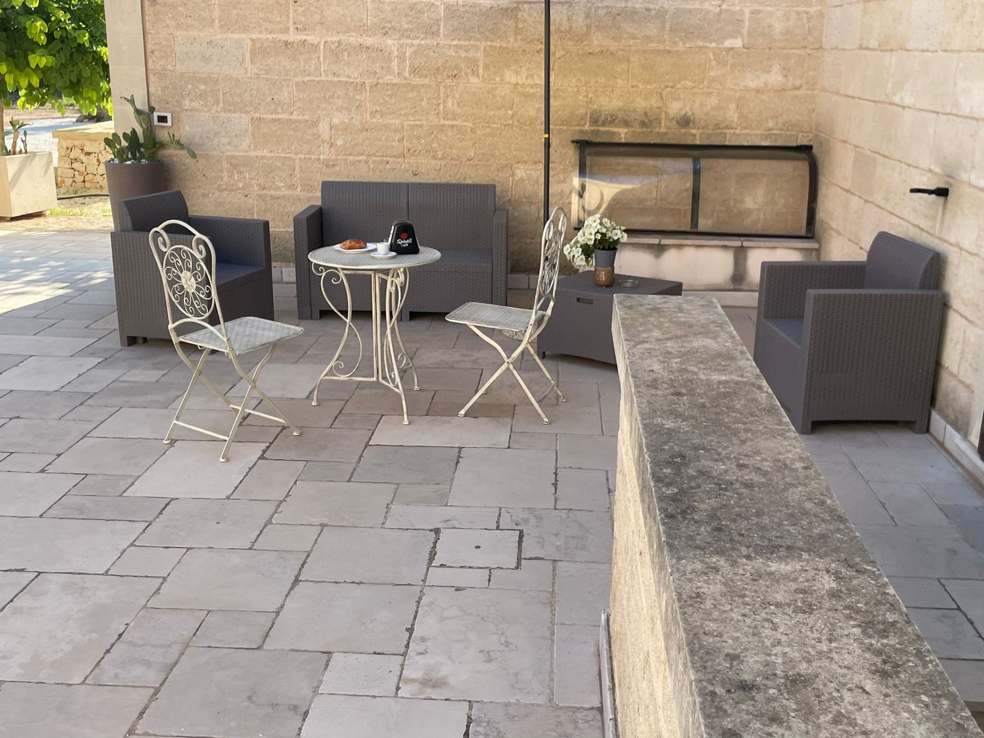 Patio esterno con mobili grigi, tavolo rotondo e pavimento in pietra.