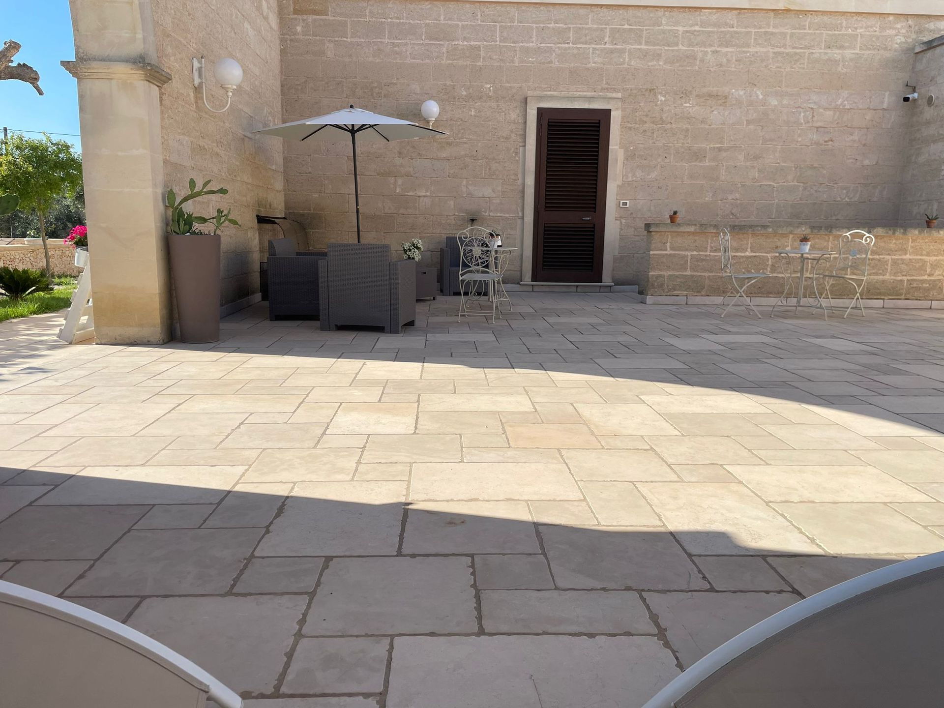 Patio con piastrelle in pietra chiara, ombrellone e posti a sedere di fronte a un edificio in pietra
