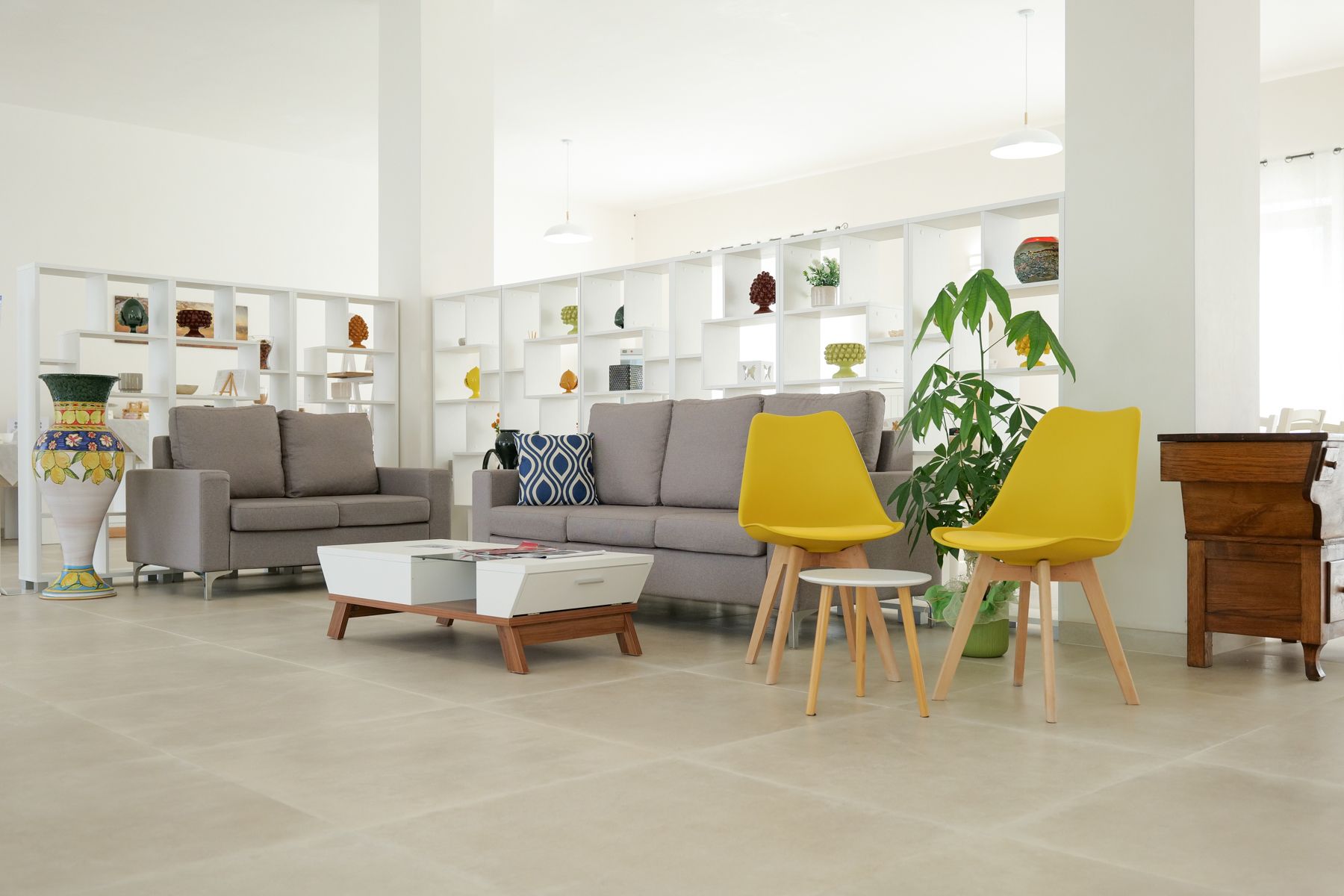 Moderna sala d'attesa con divani grigi, sedie gialle, un tavolino bianco e scaffali decorativi.