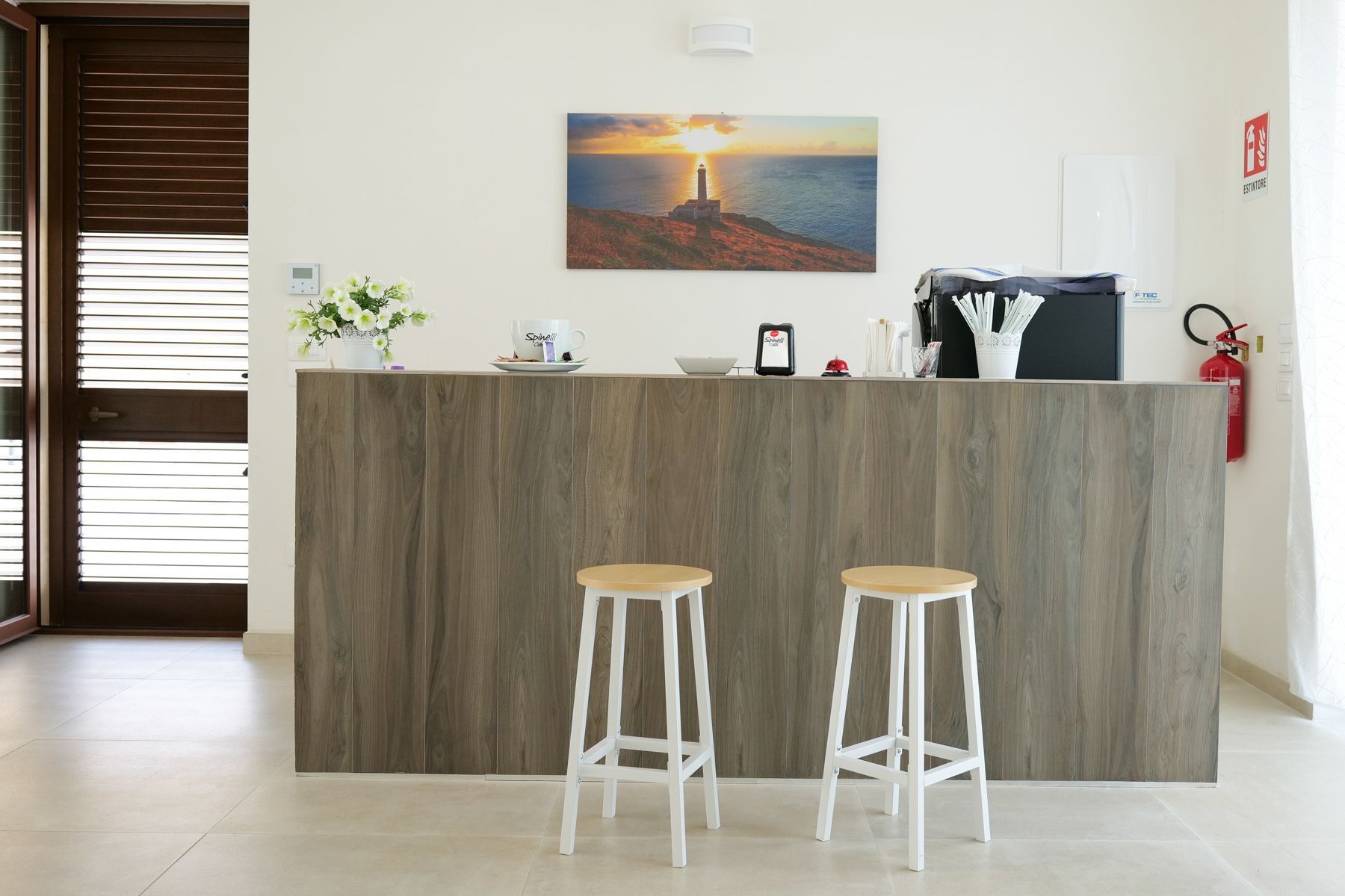 Bancone della reception con due sgabelli, un quadro e un estintore.