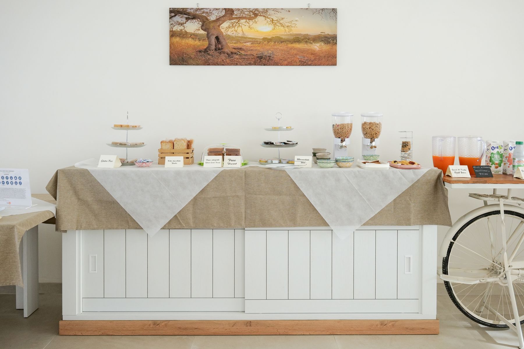 Colazione a buffet con pasticcini, cereali e bevande su un bancone bianco con un runner da tavolo in tela di iuta.
