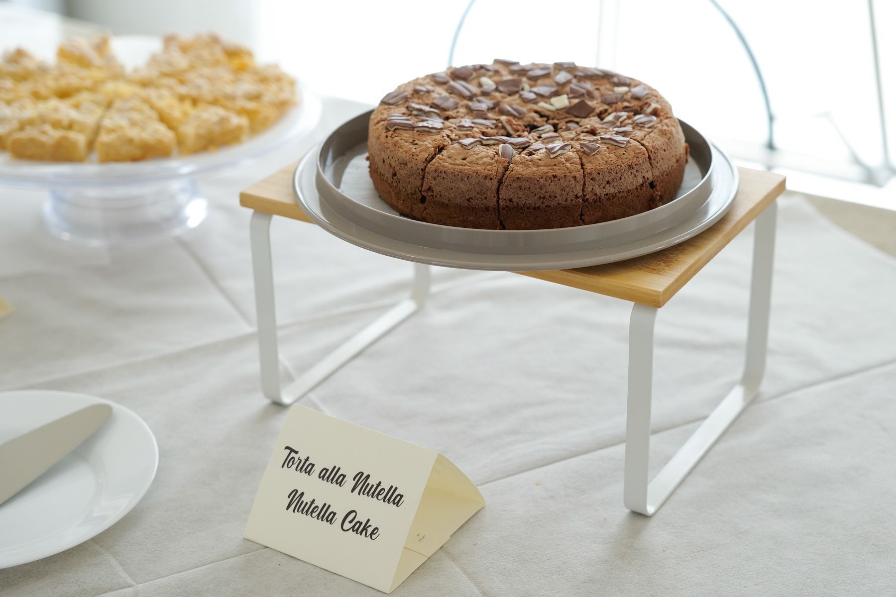 Torta su un piccolo supporto, apparecchiata al tavolo. Il testo recita 