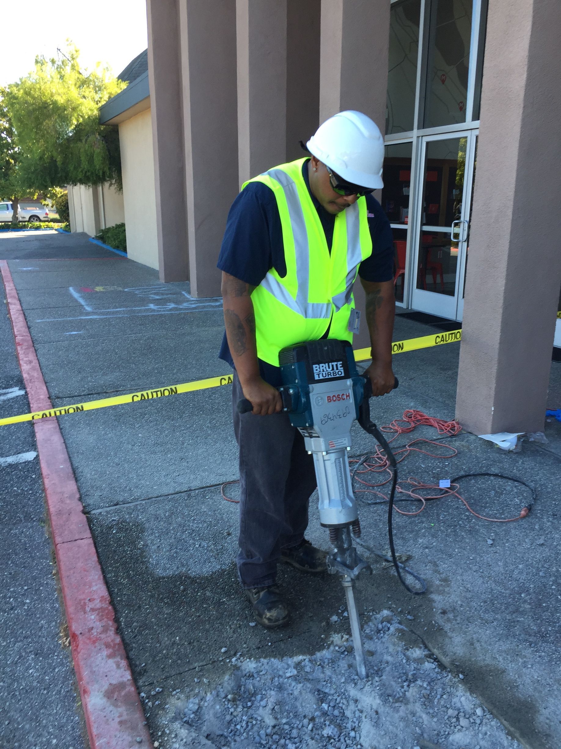 A man wearing a hard hat is using a hammer on a sidewalk