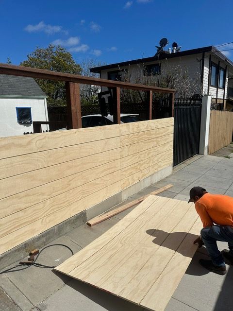 A man in an orange shirt is working on a wooden fence